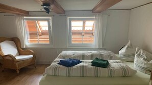 Quarto com cama, duas janelas, uma cadeira e um radiador.