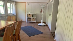 Quarto com mesa de jantar de madeira, cadeiras, tapete azul, prateleira branca com cestos e pedestal branco com design de coroa.