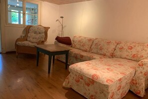 A room with a wooden floor, a floral sofa, a wicker chair, and a small table. - Holiday apartment with 1 bedroom (Kleines Wiesental - Neuenweg)