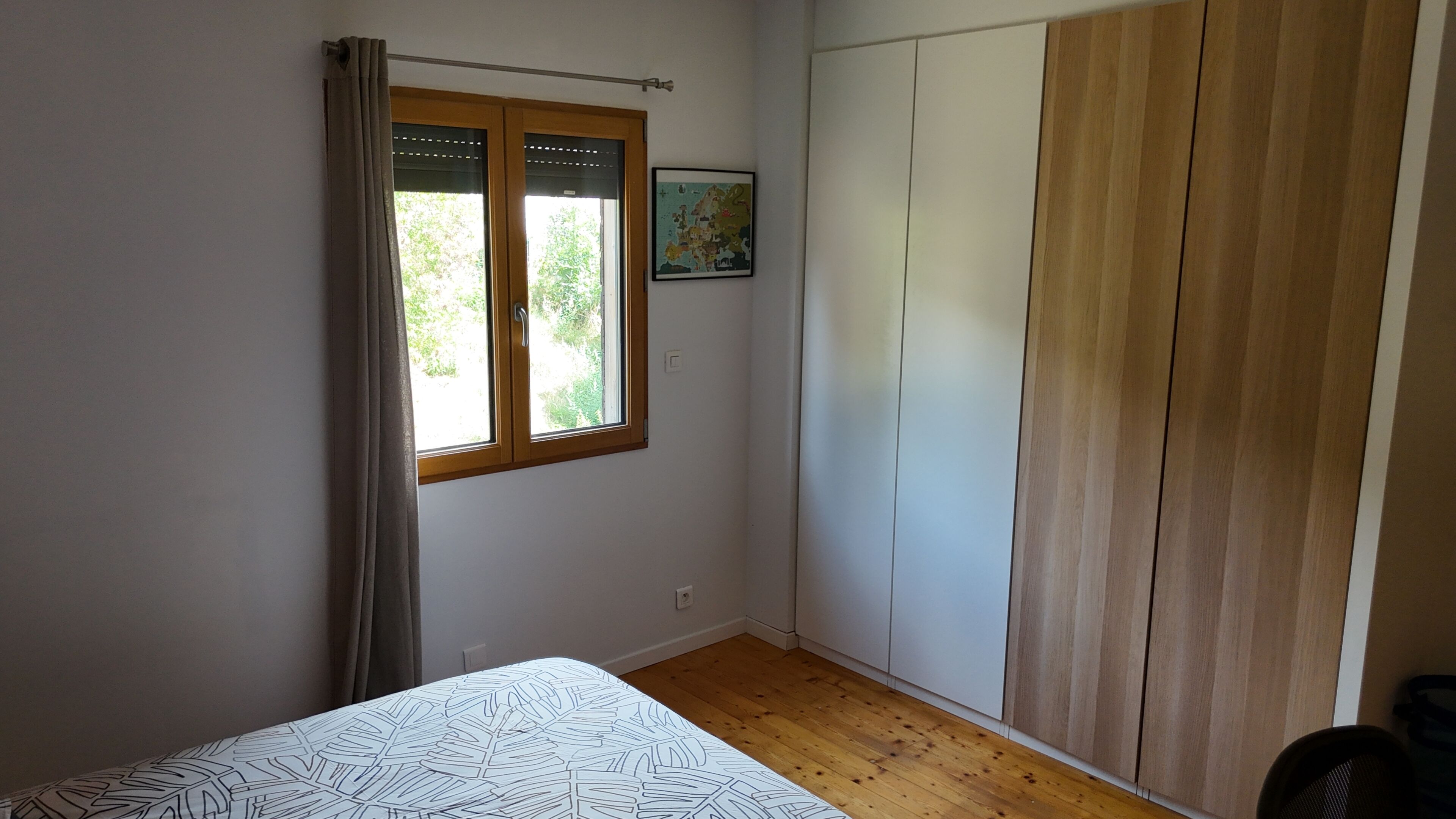 Une chambre à coucher avec un lit, une fenêtre avec des rideaux, une armoire et une carte accrochée au mur.
