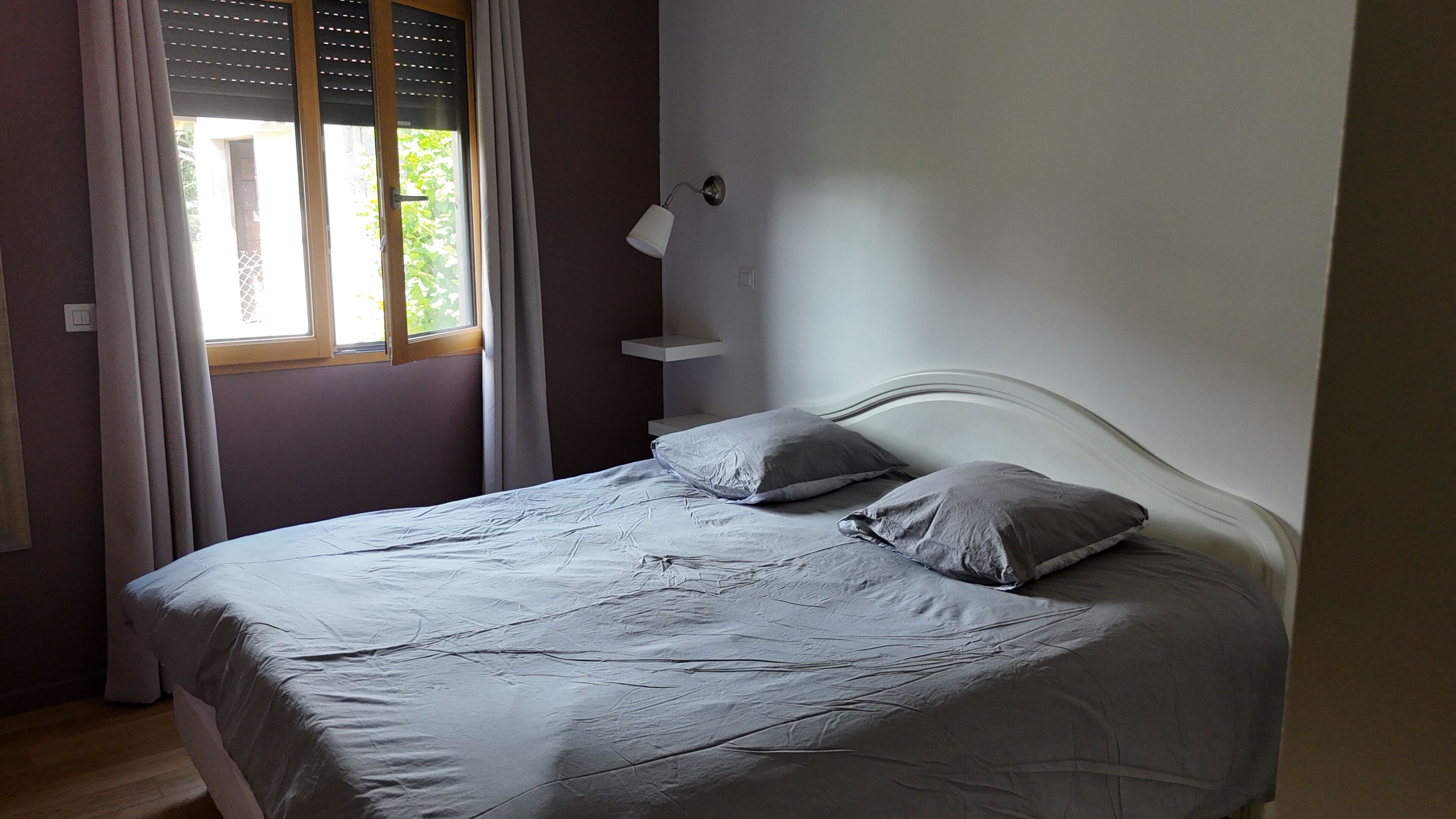 Une chambre à coucher avec un lit, une table de chevet, une lampe et une fenêtre avec des rideaux.