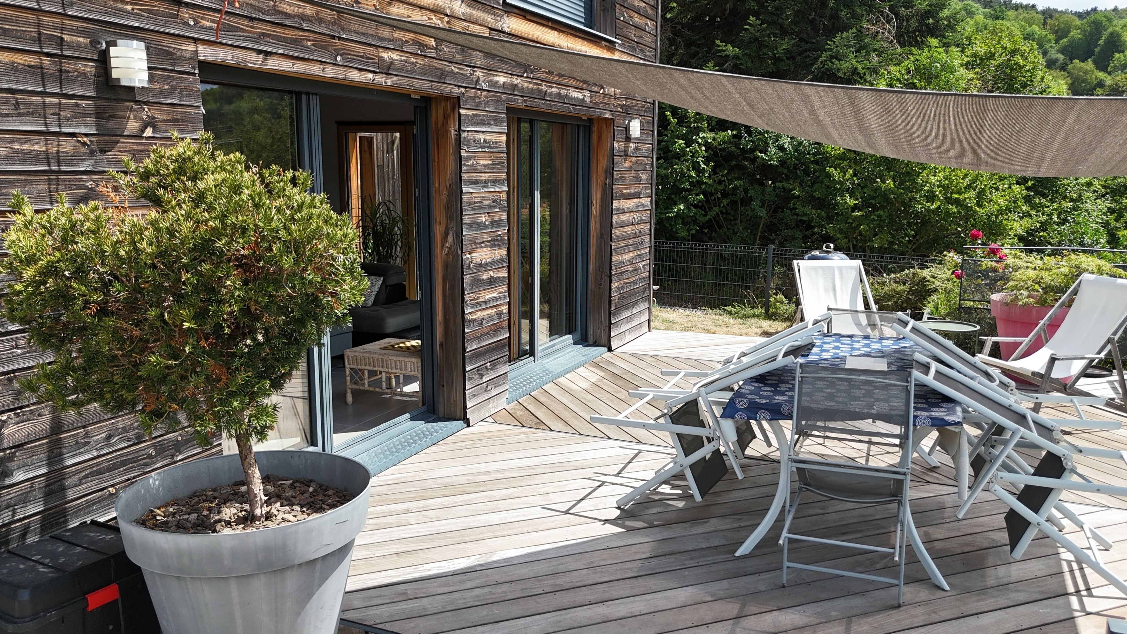 A wooden deck with a table and chairs, a potted tree, and a building with glass doors.