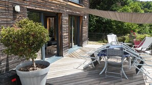 A wooden deck with a table and chairs, a potted tree, and a building with glass doors. - Bright wooden house with a view of the lake and volcanoes (Aydat)