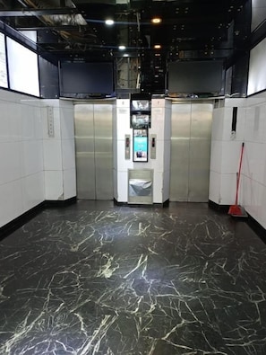 An elevator area with a marble floor, a red broom, and a digital display. - Everest Base Camp (Kowloon)