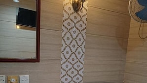 Una habitación de hotel con una cama, una mesita de noche con lámpara, un ventilador de pared y un espejo.