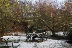 Een besneeuwde buitenplaats met een houten bank en een huifkar.