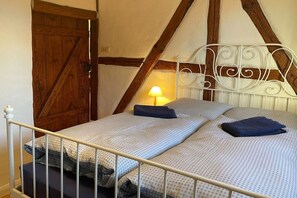 A single bed with a metal frame and white bedding, a wooden door, and a wall with exposed beams. - Holiday Farm Smokehouse 3 (Wittendörp\/OT Karft)