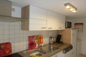A kitchen with white cabinets, a stainless steel sink, a coffee maker, and a microwave. - Holiday apartment in Wiek with Wi-Fi (Wiek)