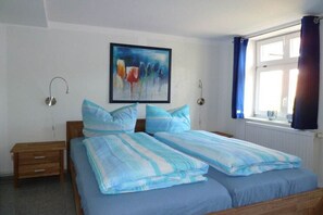 A bedroom with a bed, a nightstand, a wall-mounted lamp, and a window with curtains. - Holiday apartment in Wiek with Wi-Fi (Wiek)