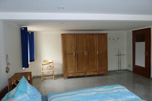 A bedroom with a bed, a wooden wardrobe, a chair, and a blue curtain. - Holiday apartment in Wiek with Wi-Fi (Wiek)