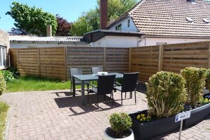 A patio with a table and chairs, a wooden fence, and a planter with plants. - Holiday apartment in Wiek with Wi-Fi (Wiek)