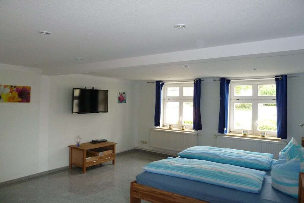 Ein Schlafzimmer mit einem Bett, einem Fernseher, einem Fenster mit Vorhängen und einer Heizung.