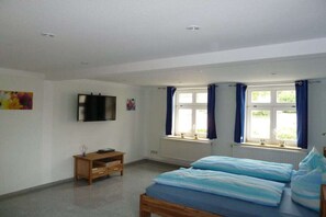 A bedroom with a bed, a television, a window with curtains, and a radiator. - Holiday apartment in Wiek with Wi-Fi (Wiek)