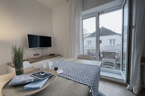 A hotel room with a bed, a TV, a dining table with a placemat, a vase with plants, and a view of the outside. - Holiday apartment Meerverliebt (Dierhagen)