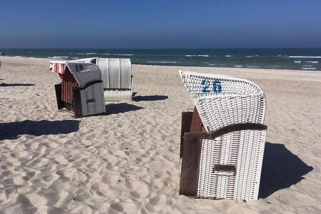 Des chaises de plage, chacune portant un numéro, sont disposées sur une plage de sable, avec l’océan en arrière-plan.