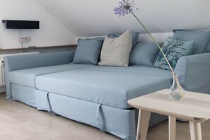 A light blue sofa with a white cushion, a small table with a vase, and a wall-mounted TV. - Holiday apartment Meerverliebt (Dierhagen)