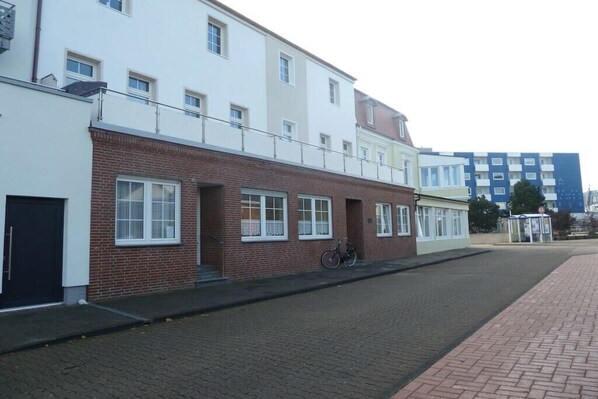 A two-story building with a brick facade, a bicycle parked outside, and a paved street. - Holiday apartment with 1 bedroom (Norderney)