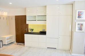 A modern kitchen with white cabinetry, a wooden door, and a small countertop with a plant. - Holiday apartment with 1 bedroom (Norderney)