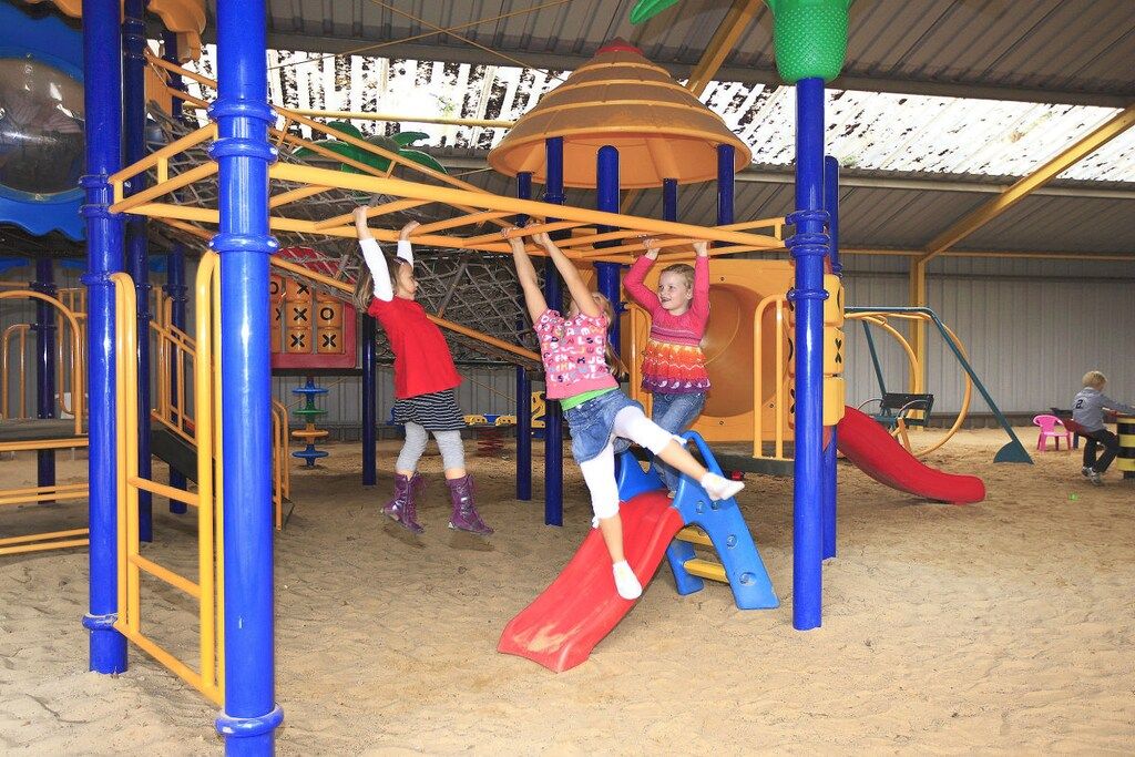 A playground with a red slide, climbing structures, and a covered play area.