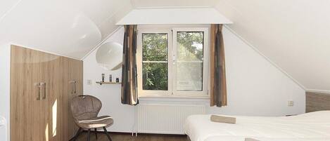 A bedroom with a bed, a chair, a wardrobe, a window, and a radiator.
