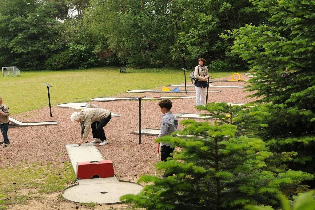 An outdoor recreational area with a shuffleboard table, a person playing shuffleboard, and another person observing.