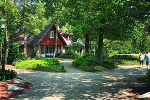 A red building with a sloped roof, surrounded by lush greenery and a paved pathway. - Wellness Superior 6/8-P (DEURNINGEN)