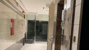 A corridor with a glass door, a telephone, and a trash bin. - Alamaan Servised Apartment  (Madinah)