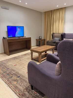 Una sala de estar con televisión, una mesa de centro, un sofá, una alfombra y una ventana con cortinas.