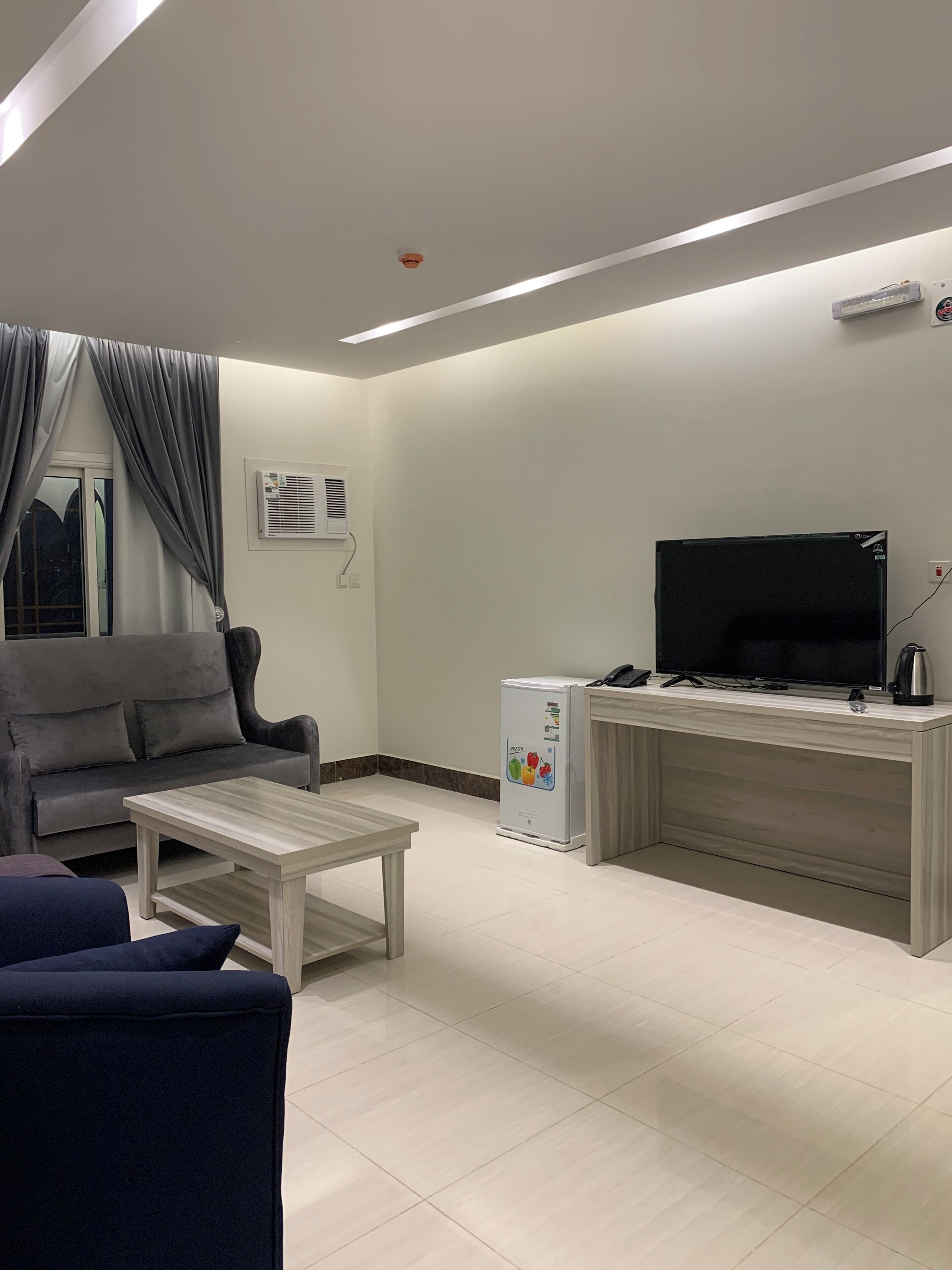 Una sala de estar moderna con un sofá, una mesa de centro, un televisor y un refrigerador.