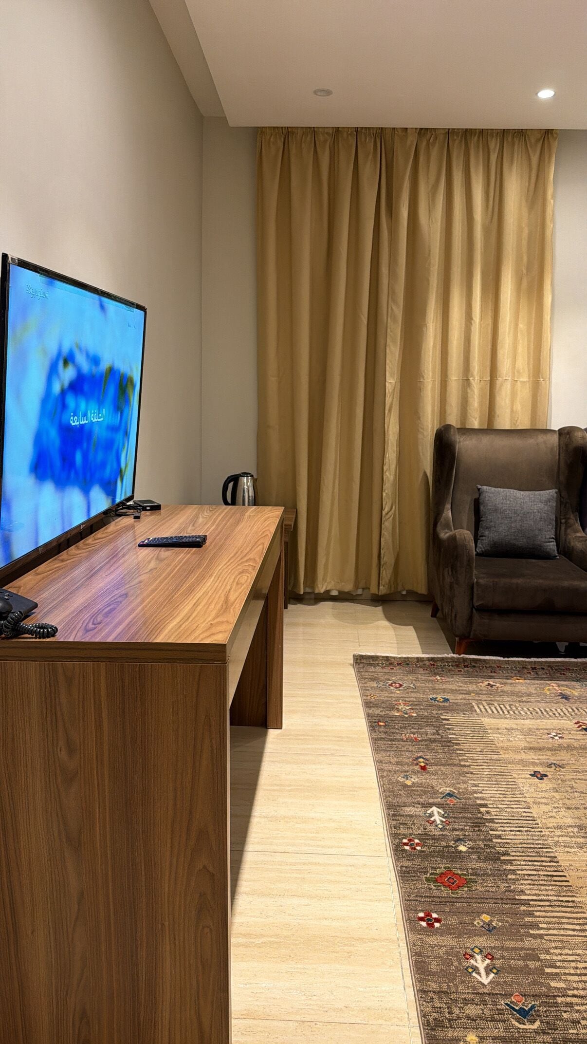 A modern living room with a wooden desk, a television, a sofa, a coffee maker, and a patterned rug.