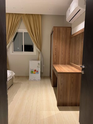 A compact kitchen with a refrigerator, wooden cabinets, and a window with curtains.