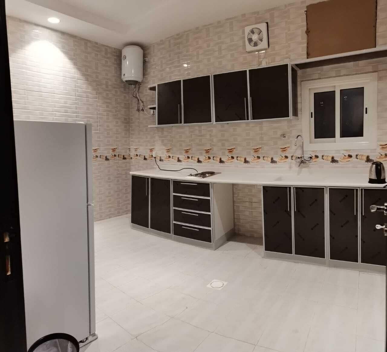 Una cocina con encimera blanca, armarios negros y salpicadero de azulejos.