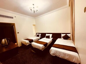 A hotel room with three single beds, a wooden nightstand, a kettle, and a door leading to another room.