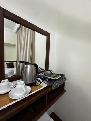 A hotel room with a wooden side table holding a kettle, teapots, and a remote control. - ofok kenda hotel (Makkah)