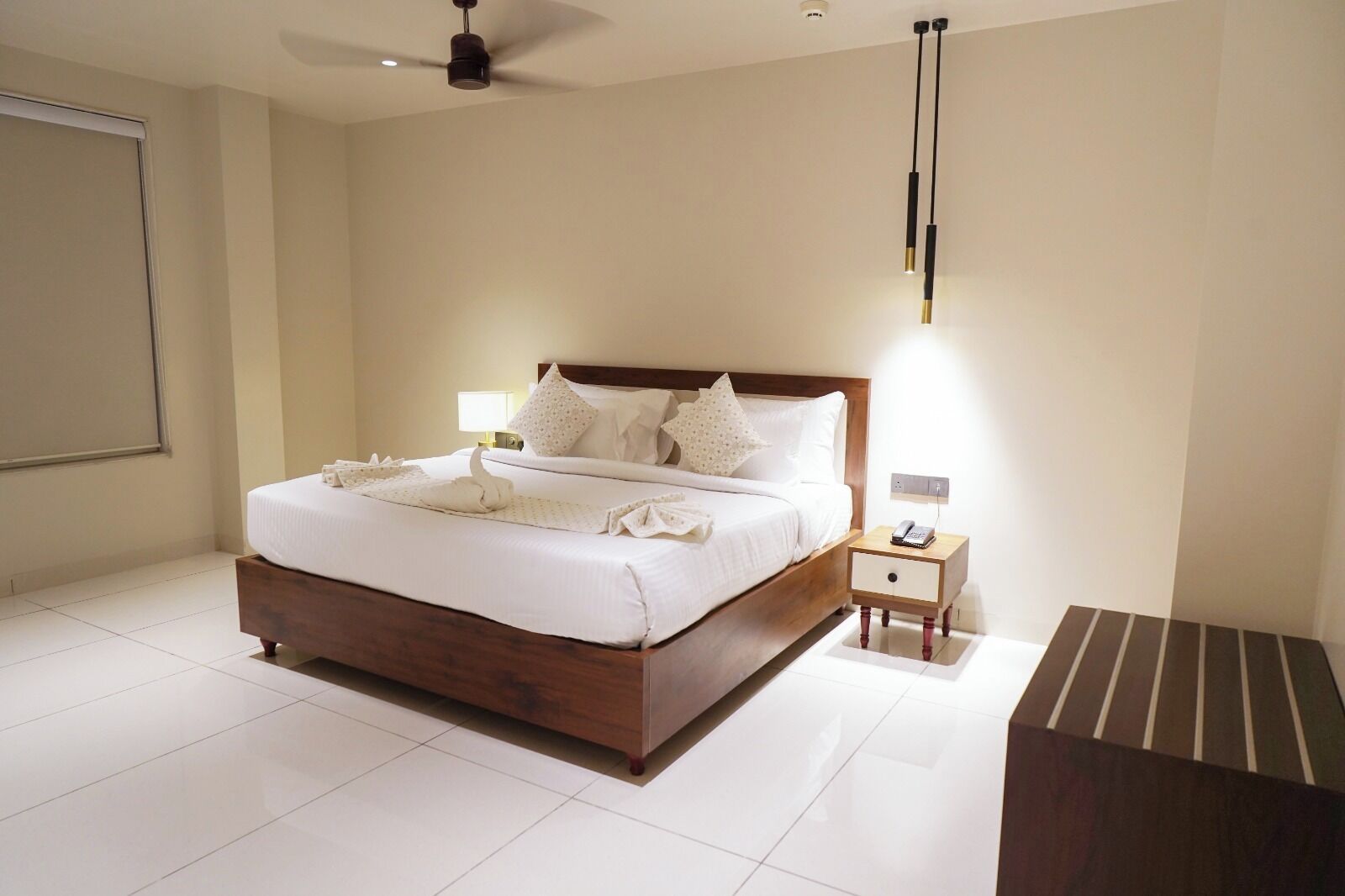 A hotel room with a large bed, a bedside table with a lamp, a ceiling fan, and a modern light fixture.
