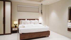 A hotel room with a large bed, a nightstand with a lamp, a wardrobe, and a mirror. - Kashi Courtyard (Varanasi)