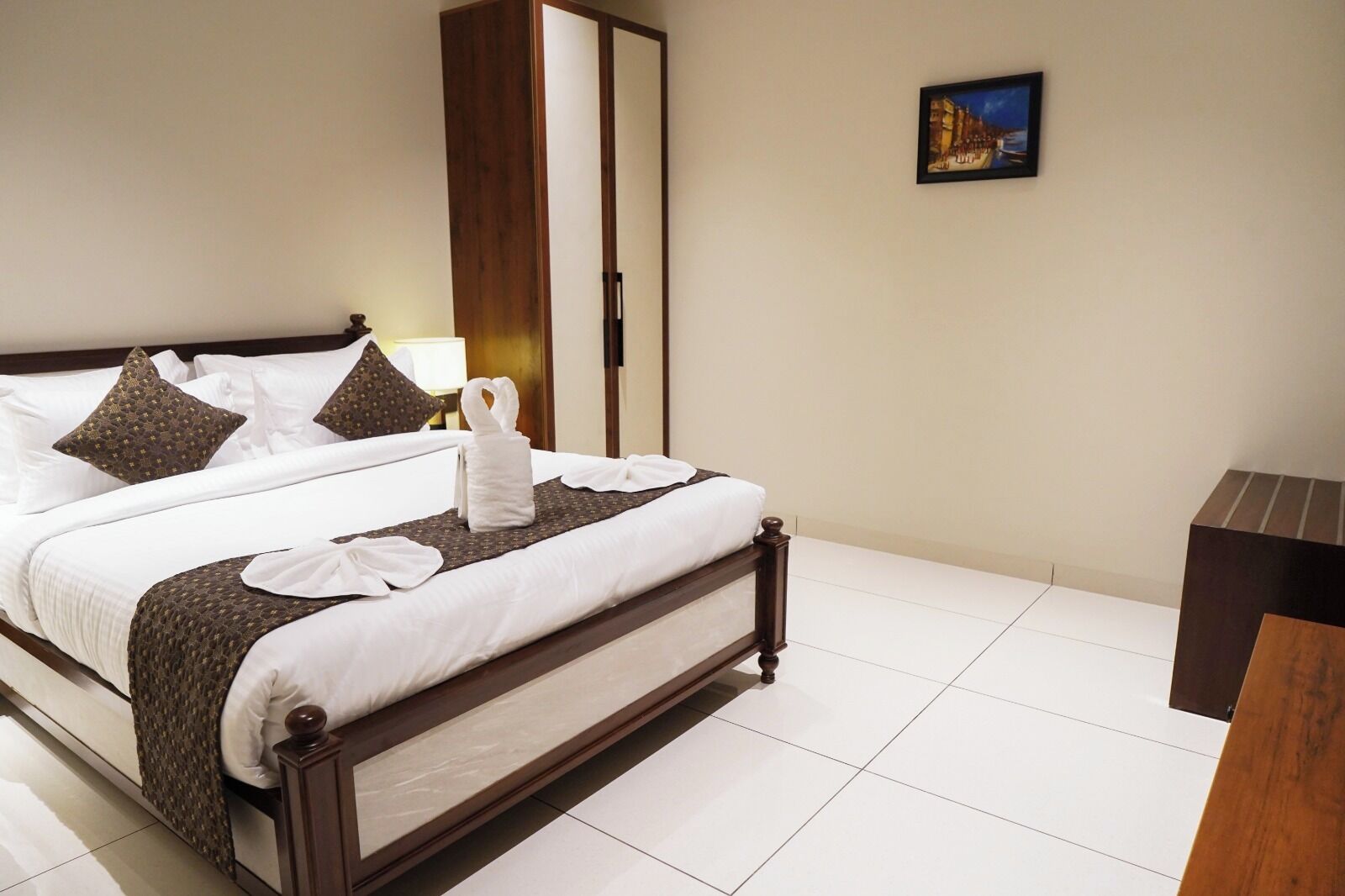 A hotel room with a bed, a wardrobe, a bedside table, and a painting on the wall.