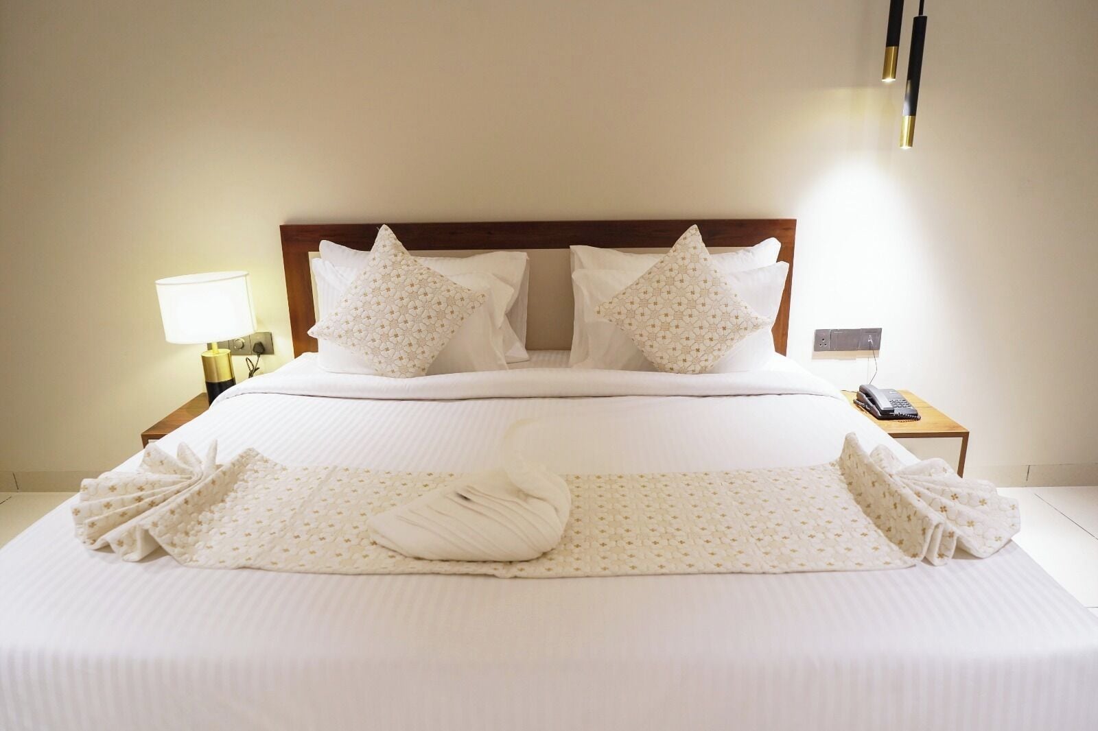 A neatly made bed with white linens and pillows, a bedside lamp, and a telephone on a wooden nightstand.