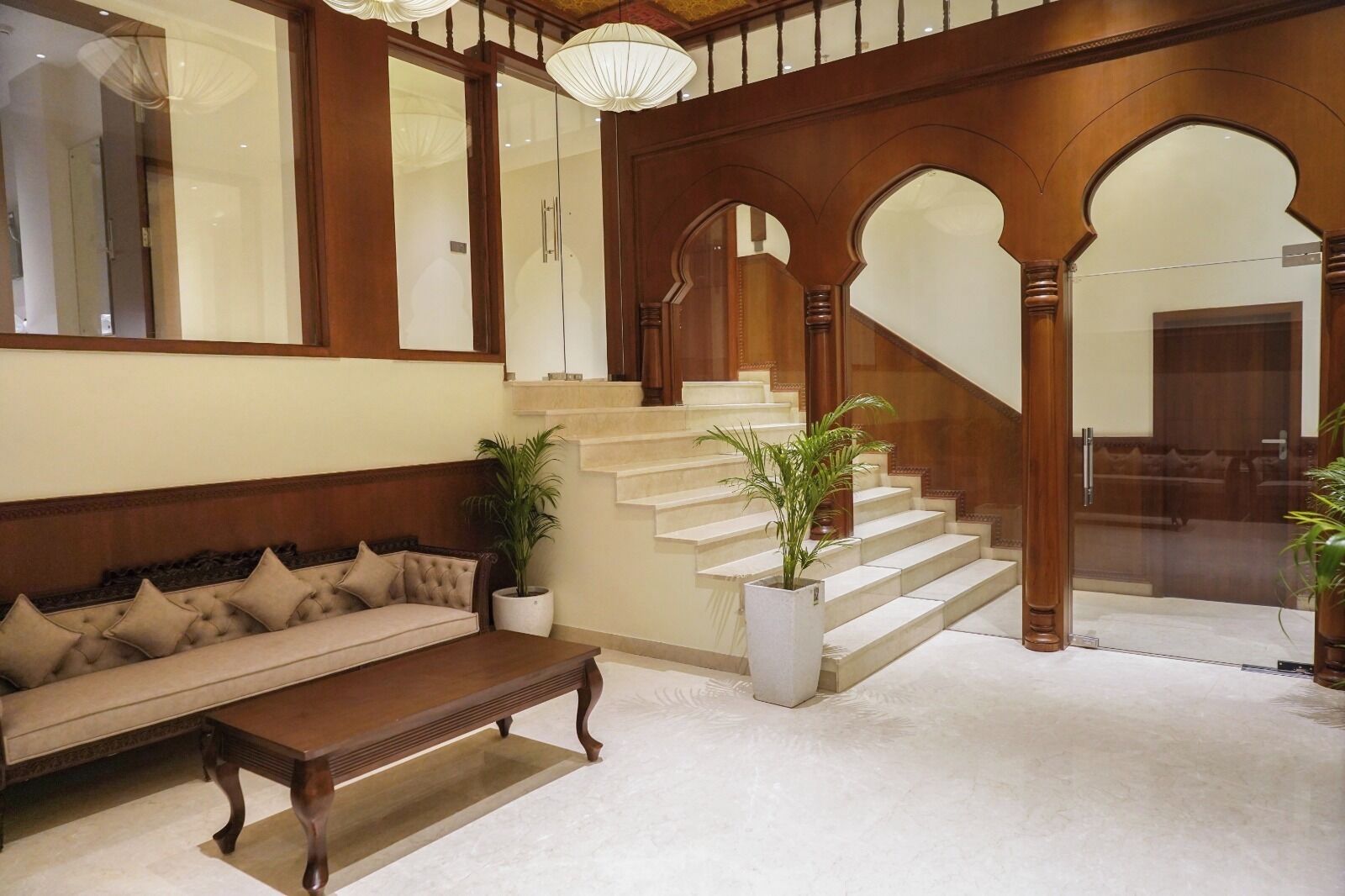 A spacious lobby with a grand staircase, a plush sofa, and potted plants.