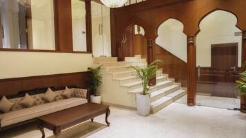 A spacious lobby with a grand staircase, a plush sofa, and potted plants.
