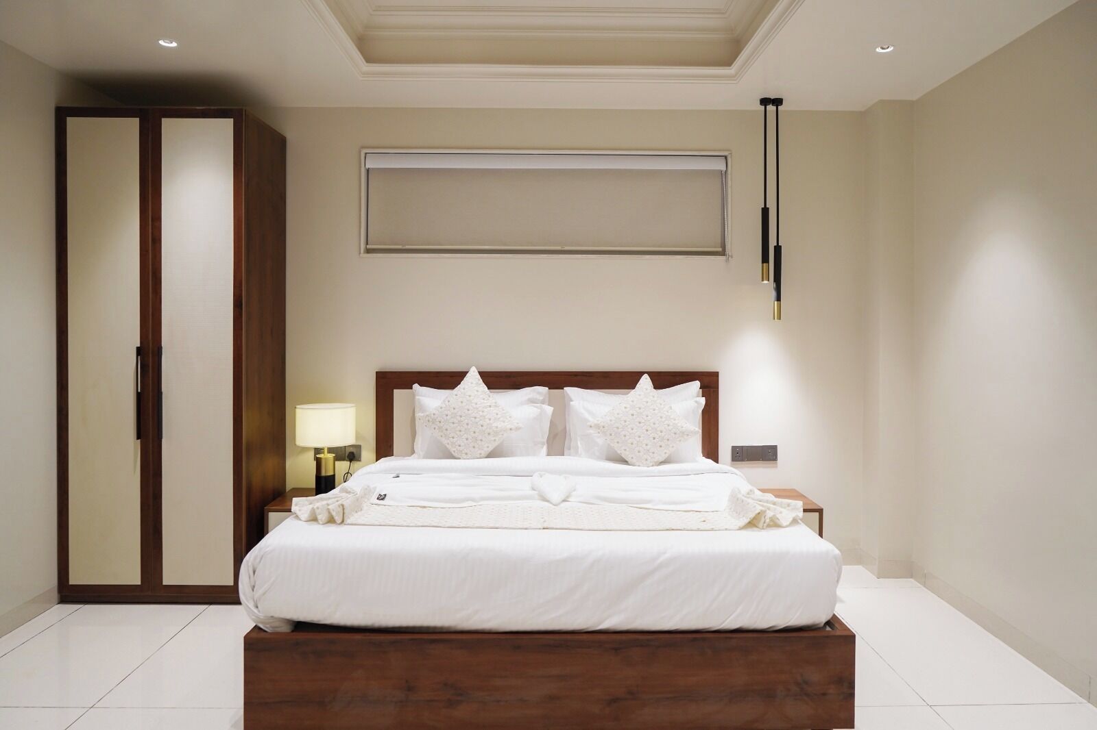 Een hotelkamer met een groot bed, een kledingkast, een nachtkastje met een lamp en een plafondlamp.