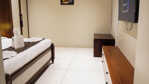 Una habitación de hotel con una cama, una mesita de noche, un televisor montado en la pared y un pequeño marco de fotos.
