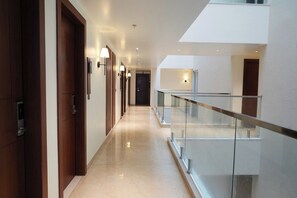 Un couloir d’hôtel moderne avec une rambarde en verre, des portes en bois et un éclairage encastré.