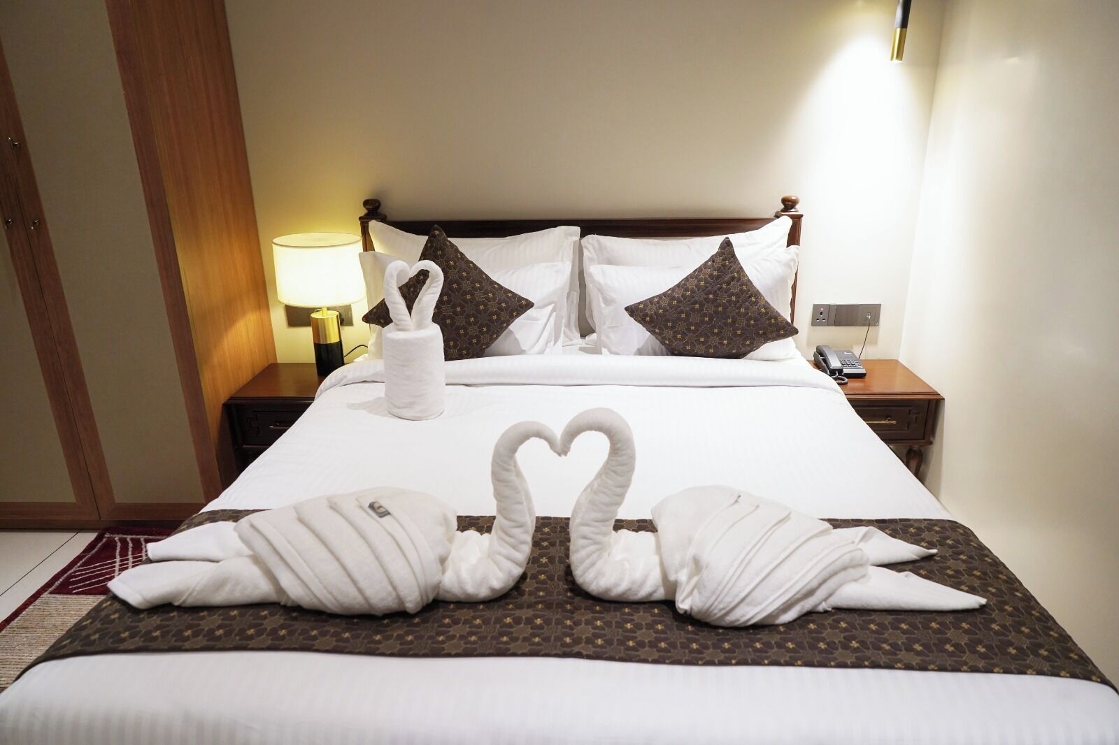 A hotel room with a neatly made bed, a bedside table with a lamp, and a wall-mounted phone.