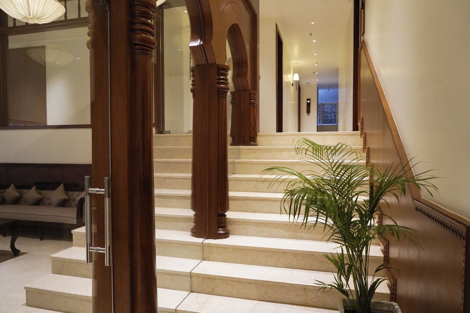 A grand staircase with wooden balusters, a potted plant, and a sofa in a well-lit hallway.