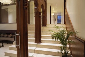 Un grand escalier avec des balustrades en bois, une plante en pot et un canapé dans un couloir bien éclairé.