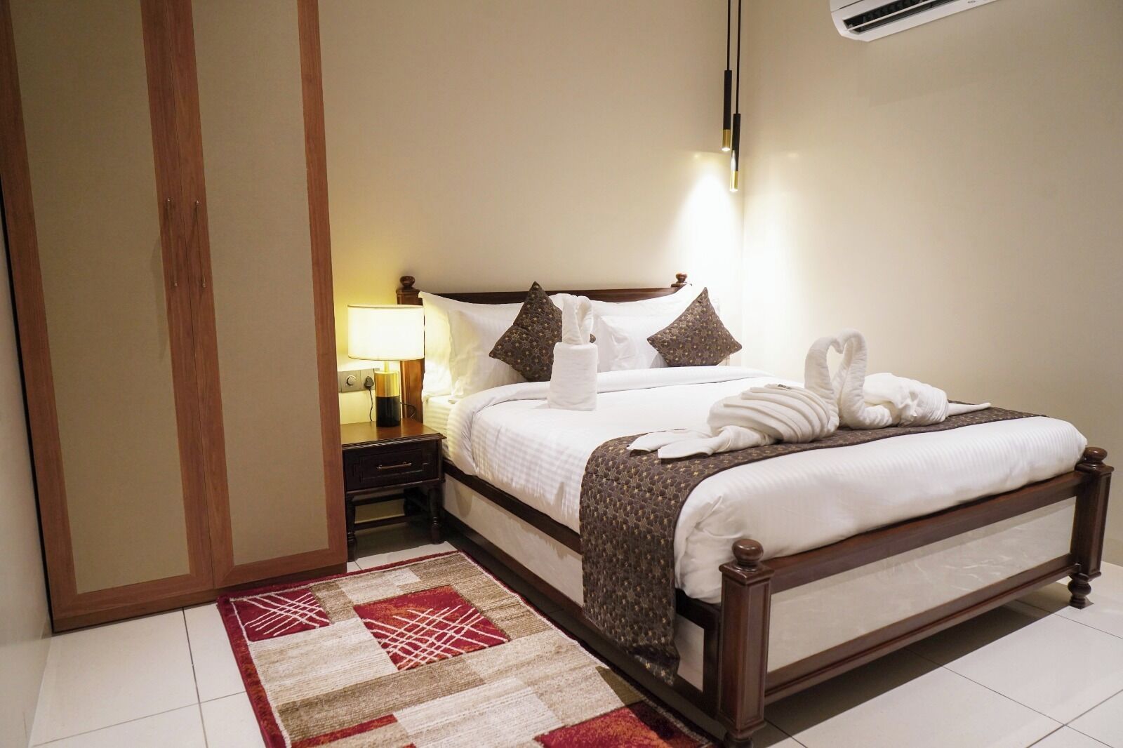 Una camera d'albergo con un letto rifatto, una lampada da comodino, un tavolino e un tappeto decorato.