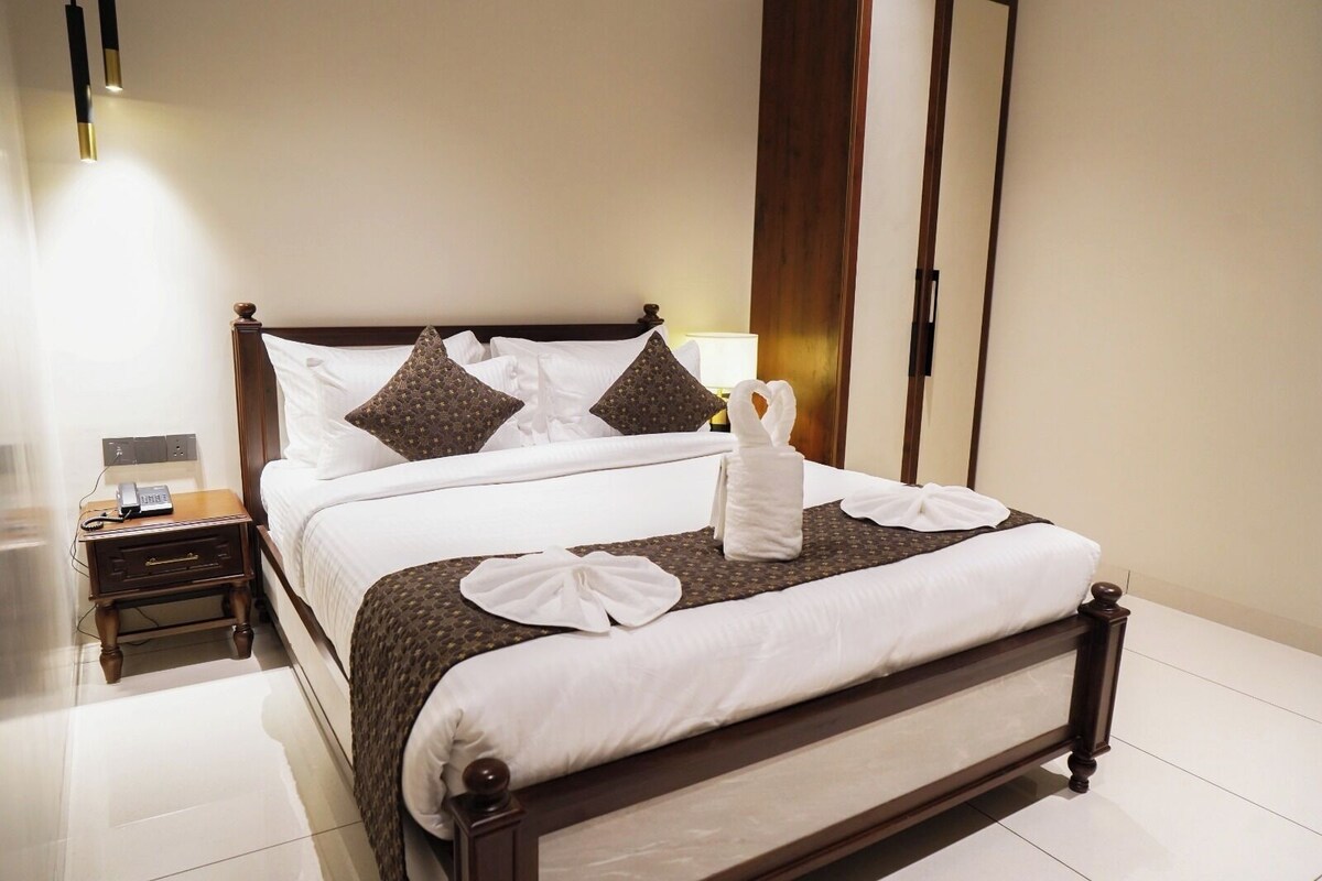 A neatly made bed with white linens, two brown patterned pillows, and a towel arranged on the bed.