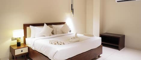 A neatly made bed with white linens, a bedside lamp, and a wooden nightstand with a drawer.