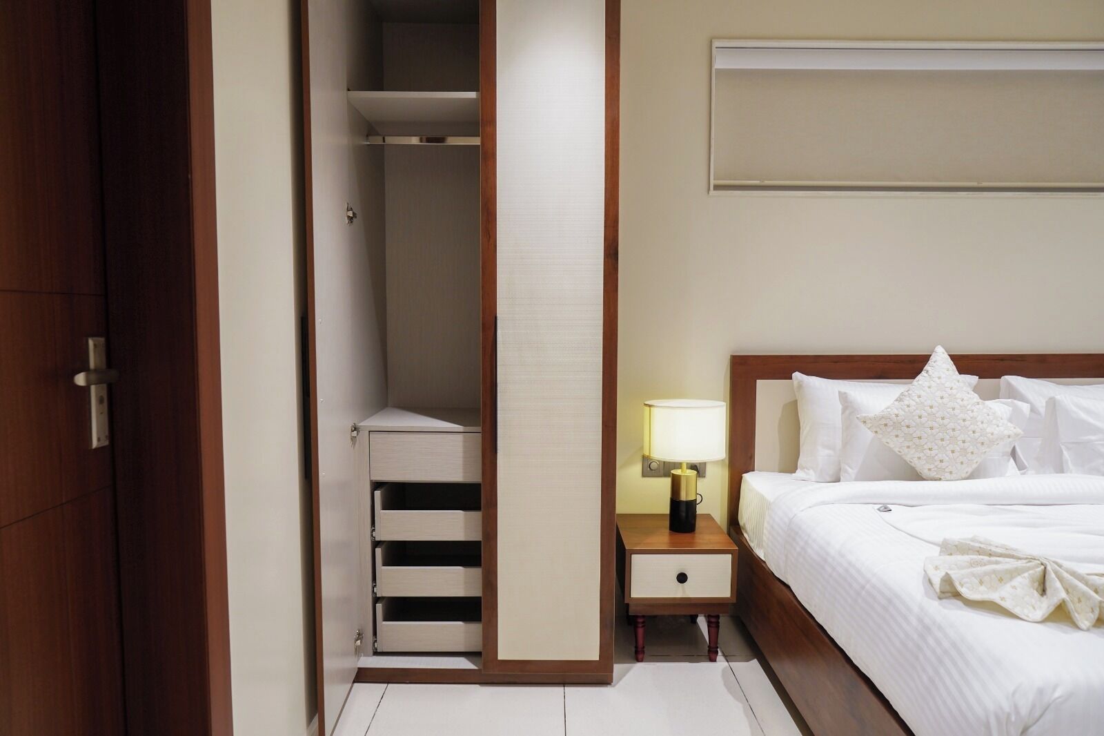 Habitación de hotel con cama, mesita de noche, lámpara y un armario con varios cajones.